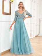 Woman wearing a blue evening gown with silver sequin top in a room.
