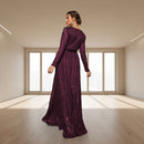 Woman in a purple evening gown standing in an elegant room with chandelier.