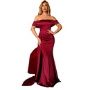 Woman in a burgundy off-shoulder gown posing against a dark background with a red couch.