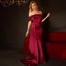 Woman in a burgundy evening gown standing against a dark background with a red couch.